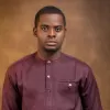 Portrait of a man wearing a maroon traditional outfit against a brown background.